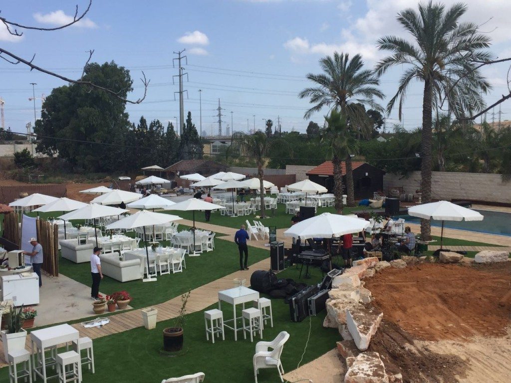 גינה מעוצבת לאירועים עם שולחנות וכסאות, דק עץ ובריכות, מוכנה להשכרת ציוד לאירועים.
