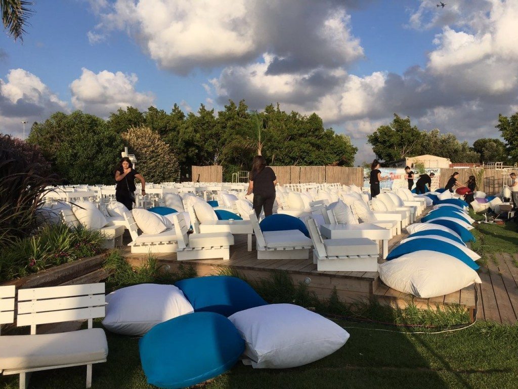 מקום לאירועים עם כסאות ושולחנות, אנשים מסדרים ריהוט ושטיחים לפני האירוע.