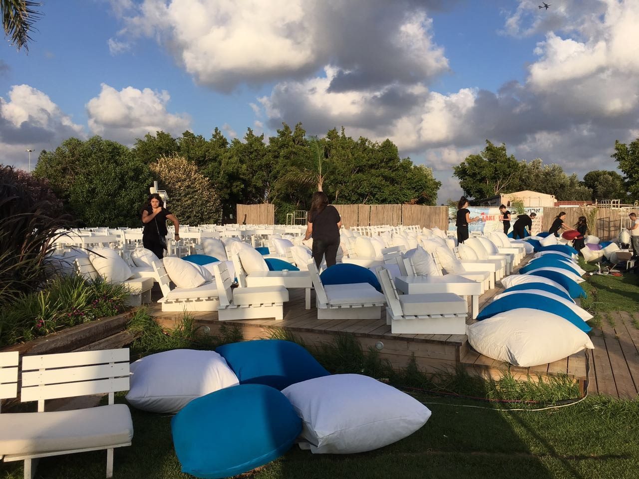 מקום לאירועים עם כסאות ושולחנות, אנשים מסדרים ריהוט ושטיחים לפני האירוע.
