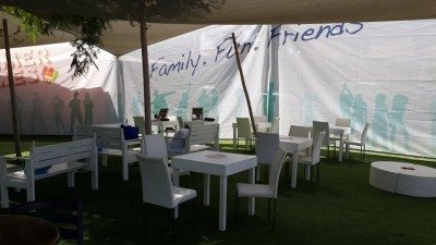 פינת ישיבה לאירועים עם שולחנות וכסאות לבנים, תחת אוהל עם קירות מעוטרים.