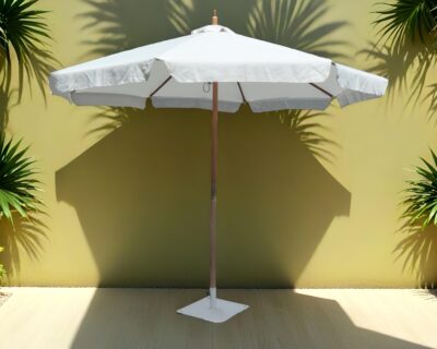 parasol לבן עומד על רצפה בהירה, עם צללים של צמחיה על הקיר מאחור.