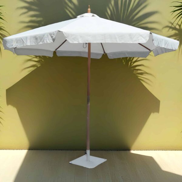 parasol לבן עומד על רצפה בהירה, עם צללים של צמחיה על הקיר מאחור.
