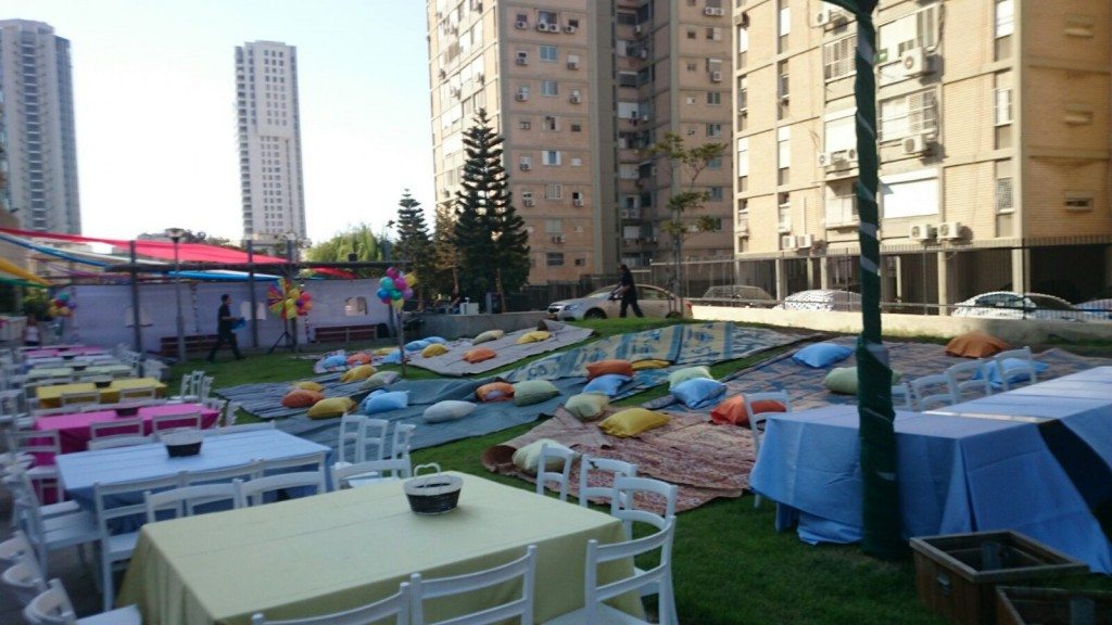 שטח אירועים מעוצב עם שולחנות וכסאות, שטיחים וכריות צבעוניות, מתאים להשכרת ציוד לאירועים.